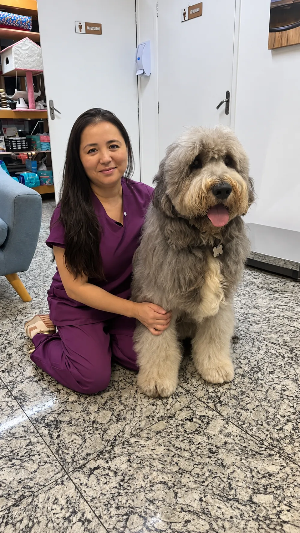 Profissional da PetLife sentada no chão da clínica ao lado de um cão de pelo longo